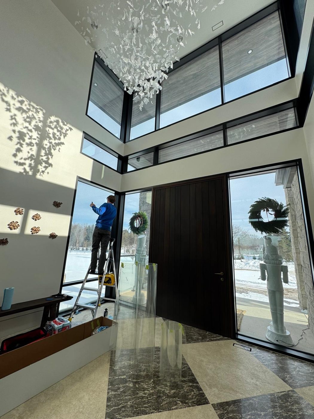Winsolux installer applying security film to full-height foyer glass beside the front door